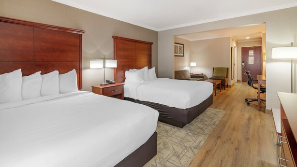Une chambre d’hôtel avec deux lits, un bureau, une chaise et une lampe.