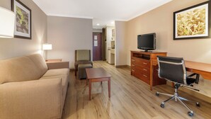 Une chambre d’hôtel avec un canapé, une petite table, un bureau avec une chaise, une télévision et des tableaux encadrés aux murs.