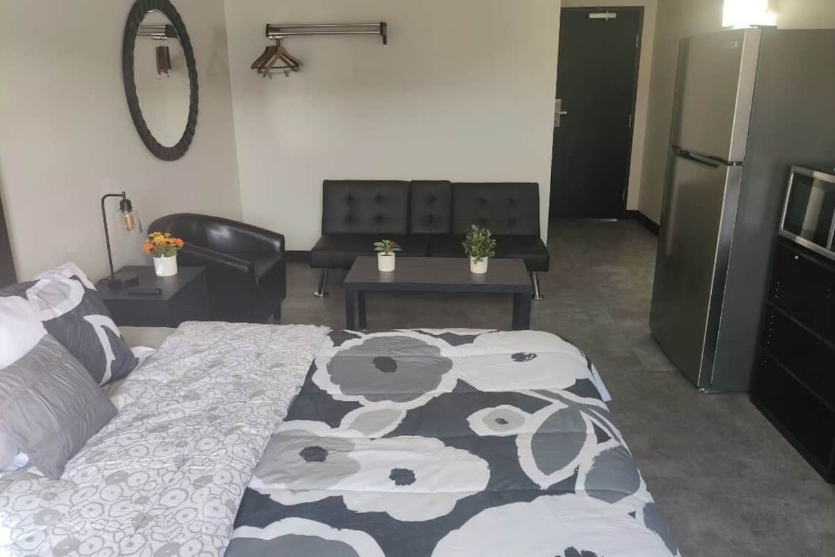 Una habitación de hotel con cama, sofá, una mesita con plantas, espejo y refrigerador.