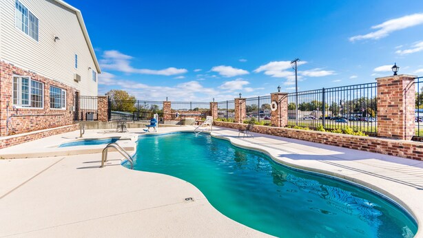 A swimming pool with a curved design, surrounded by a brick wall and a metal fence.