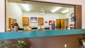 A reception area with a receptionist, wooden cabinets, a calendar, a clock, and a plant.