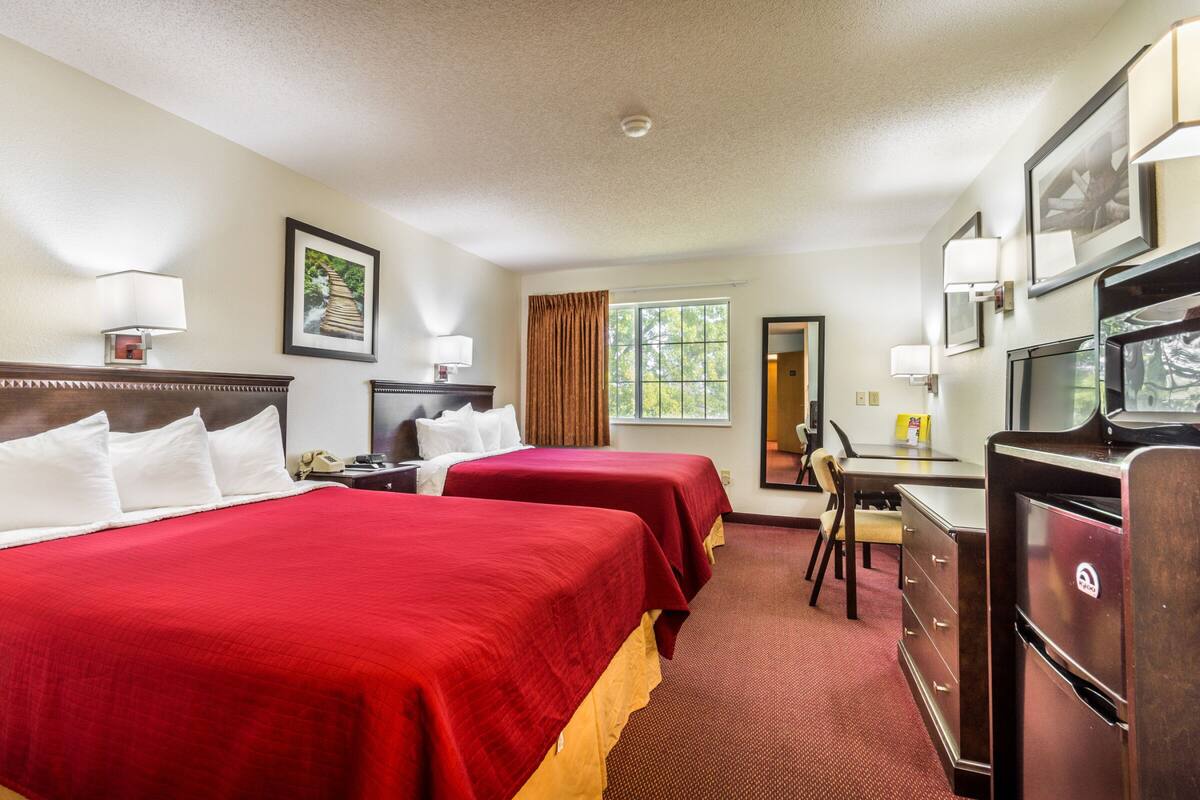A hotel room with two beds, a desk, a dresser, a television, and a window with curtains.