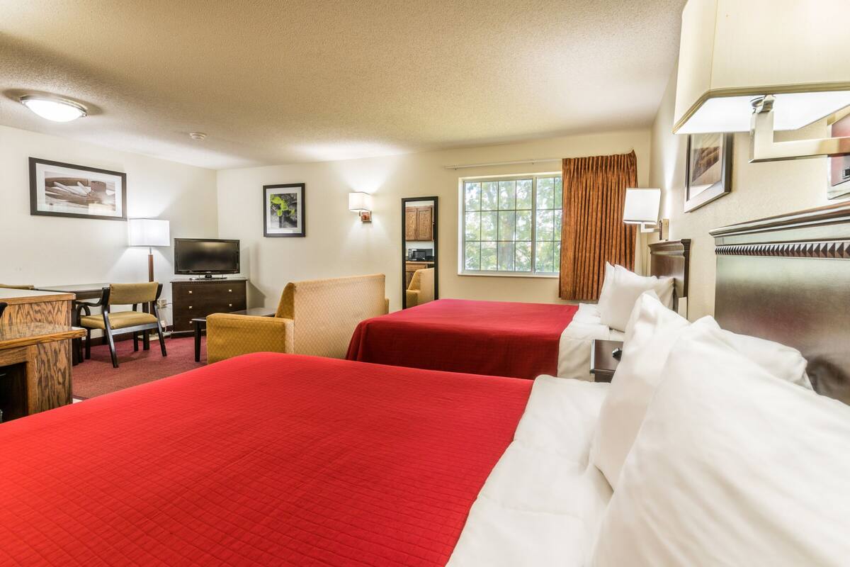 A hotel room with two beds, a desk with a chair, a television, and a window with curtains.
