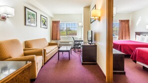 A hotel room with a sofa, a desk with a computer, a TV, and a bed with red bedding.