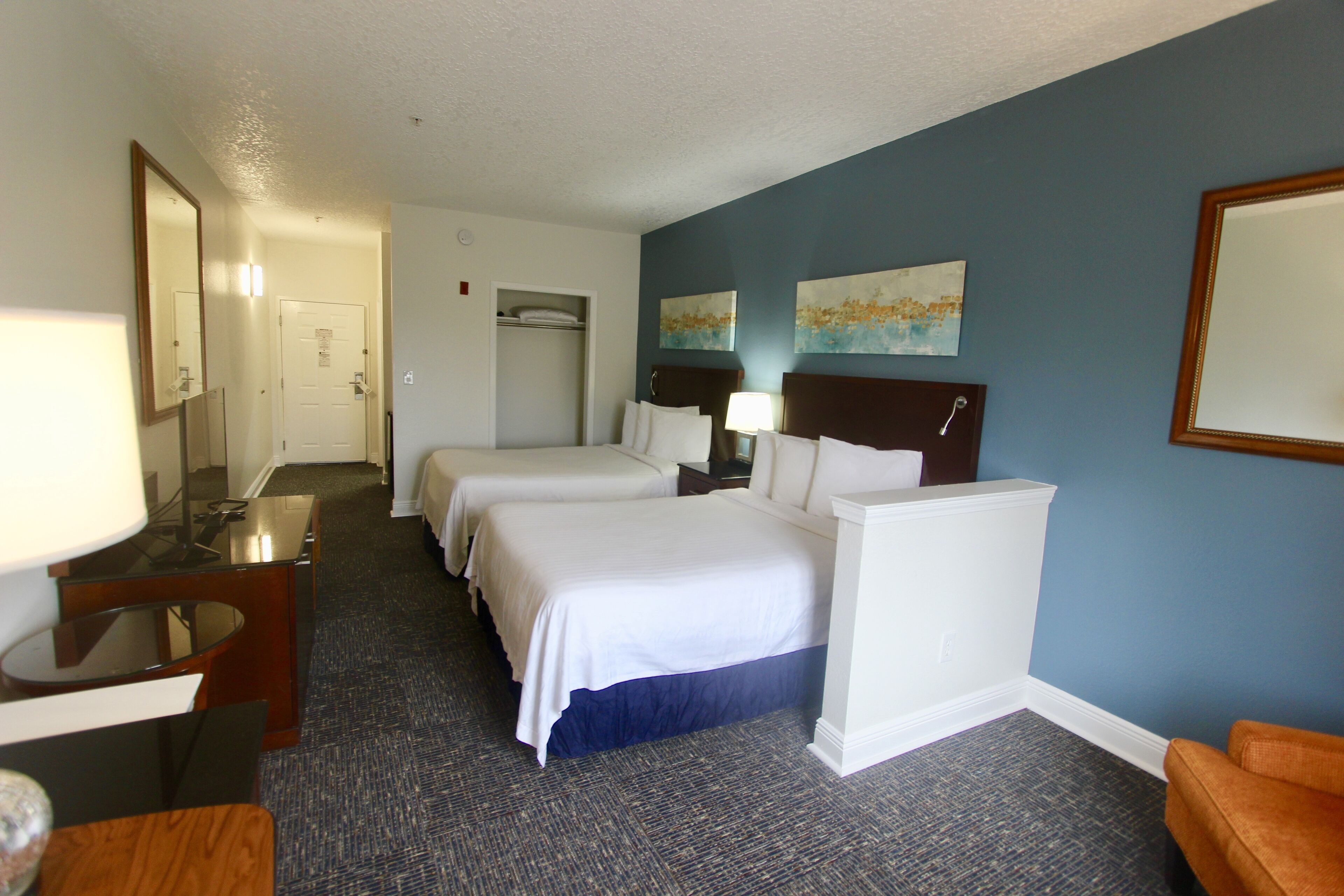 A hotel room with two beds, a desk, a chair, a mirror, and artwork on the walls.