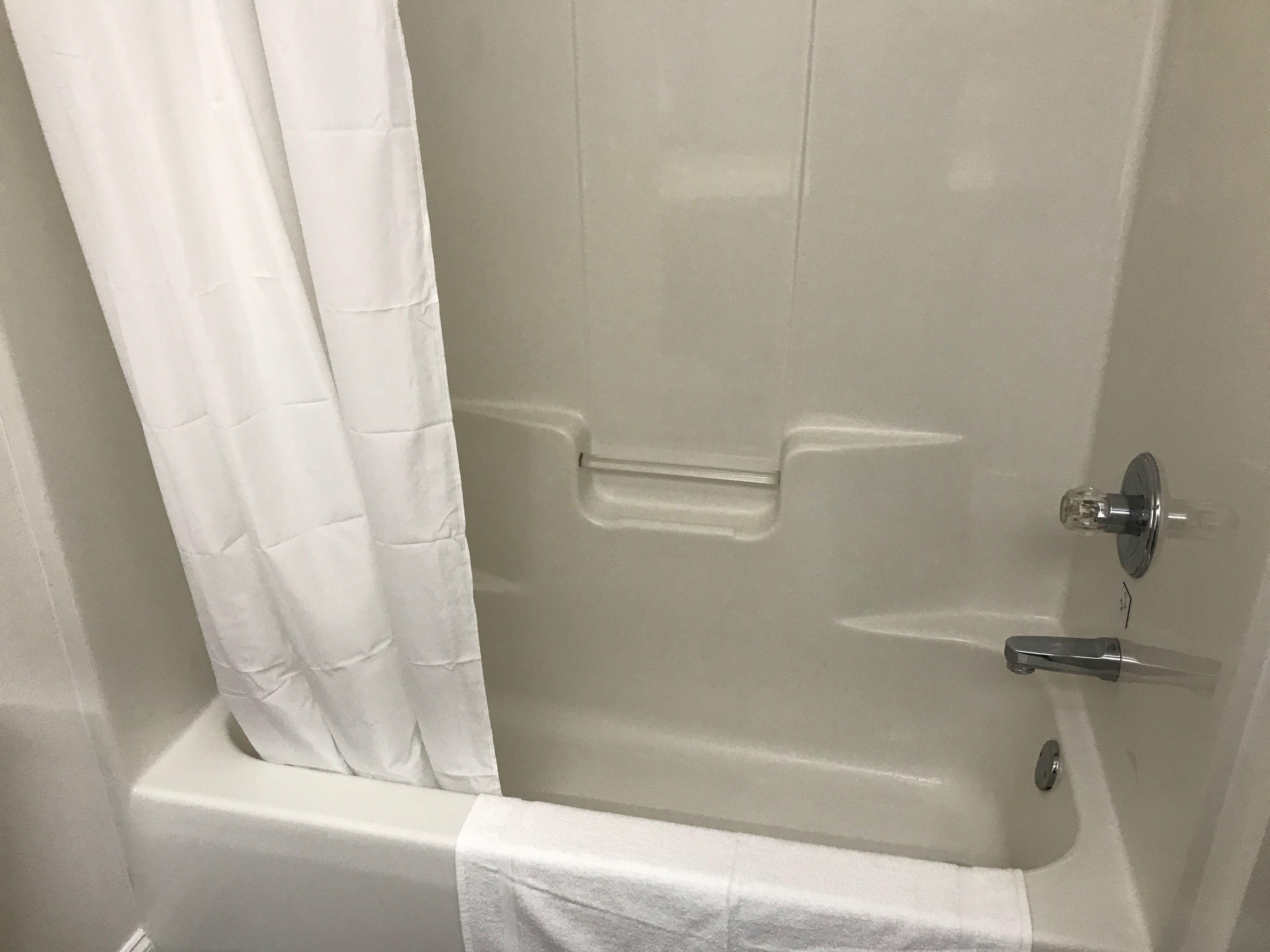 A white bathtub with a shower curtain, a faucet, and a towel rack.