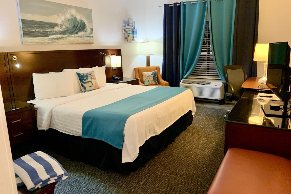A hotel room with a bed, a desk, a chair, a lamp, a TV, and a window with curtains.