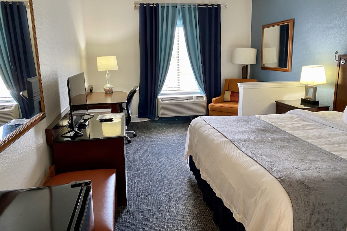 A hotel room with a bed, desk, chair, and a large mirror.