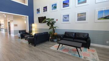 Un hall d’entrée moderne avec un mur d’accent bleu, un téléviseur à écran plat, une grande plante en pot et un espace salon avec une table basse et des canapés.