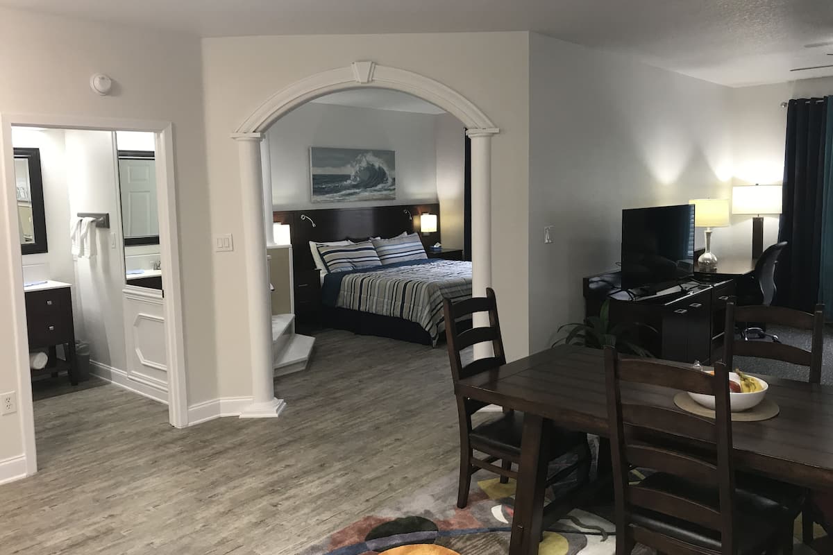 A hotel room with a bed, a desk with a computer, a TV, and a dining area with chairs and a table.