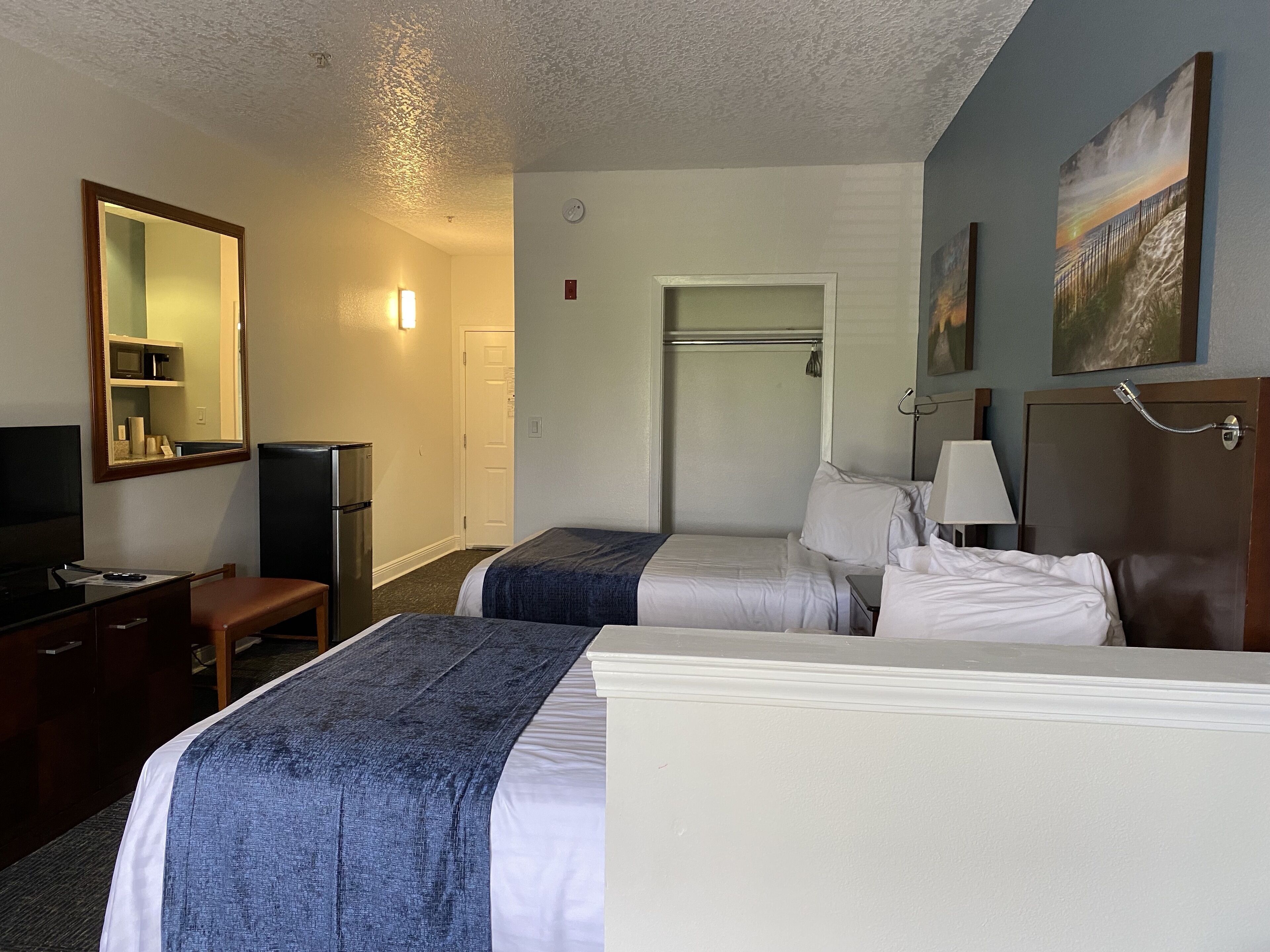A hotel room with two beds, a desk, a chair, a television, and a painting on the wall.