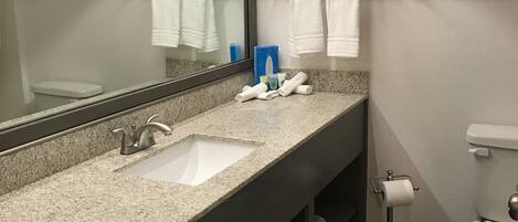 A modern bathroom with a granite countertop, two sinks, a large mirror, a toilet, and a towel rack.