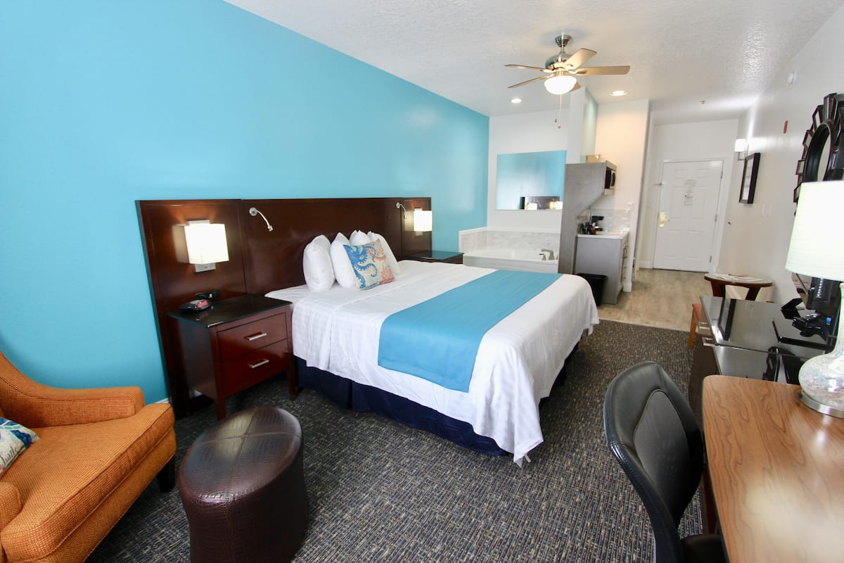 A hotel room with a bed, a desk, a chair, a sofa, a bathroom, and a ceiling fan.