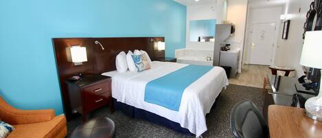A hotel room with a bed, a desk, a chair, a sofa, a bathroom, and a ceiling fan.