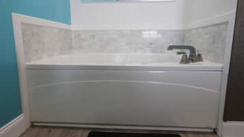 Une salle de bain avec une baignoire blanche, une fenêtre au-dessus et un tapis noir sur le sol.