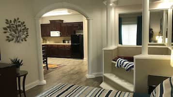 A bedroom with a large bed, a view to a kitchen, and a staircase leading to another level.