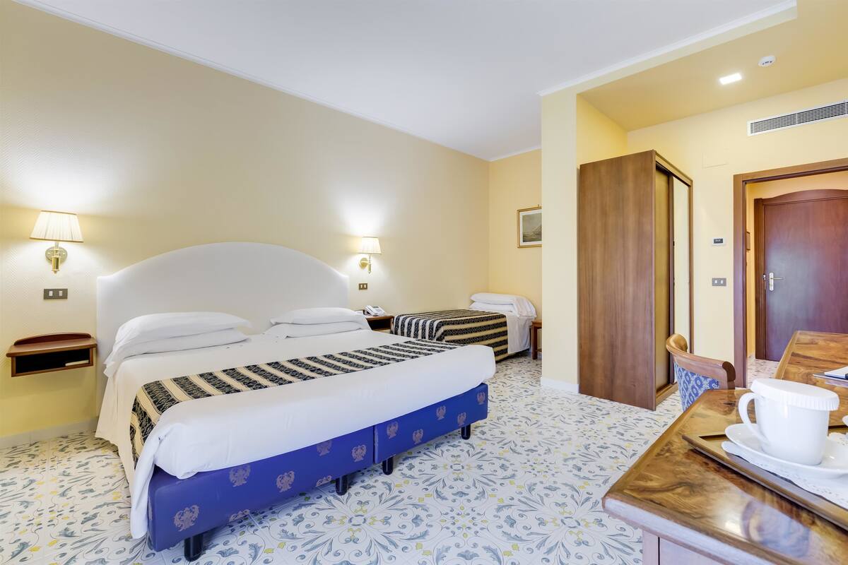 Een hotelkamer met een groot bed, een kleiner bed, een houten bureau met een kop en een vloer met een patroon.