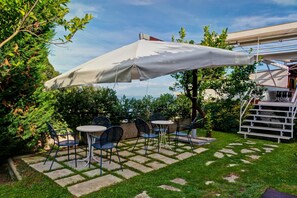 Une terrasse extérieure avec un sol en pierre, des chaises en métal et un grand parasol blanc.