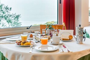 A breakfast table set with plates, cutlery, a coffee pot, and a view of the sea.
