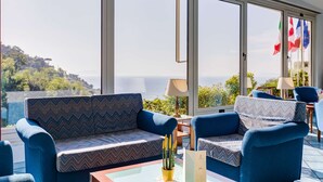 Een moderne lounge met een bank en fauteuils, grote ramen met uitzicht op zee, en vlaggen van Frankrijk en Canada.