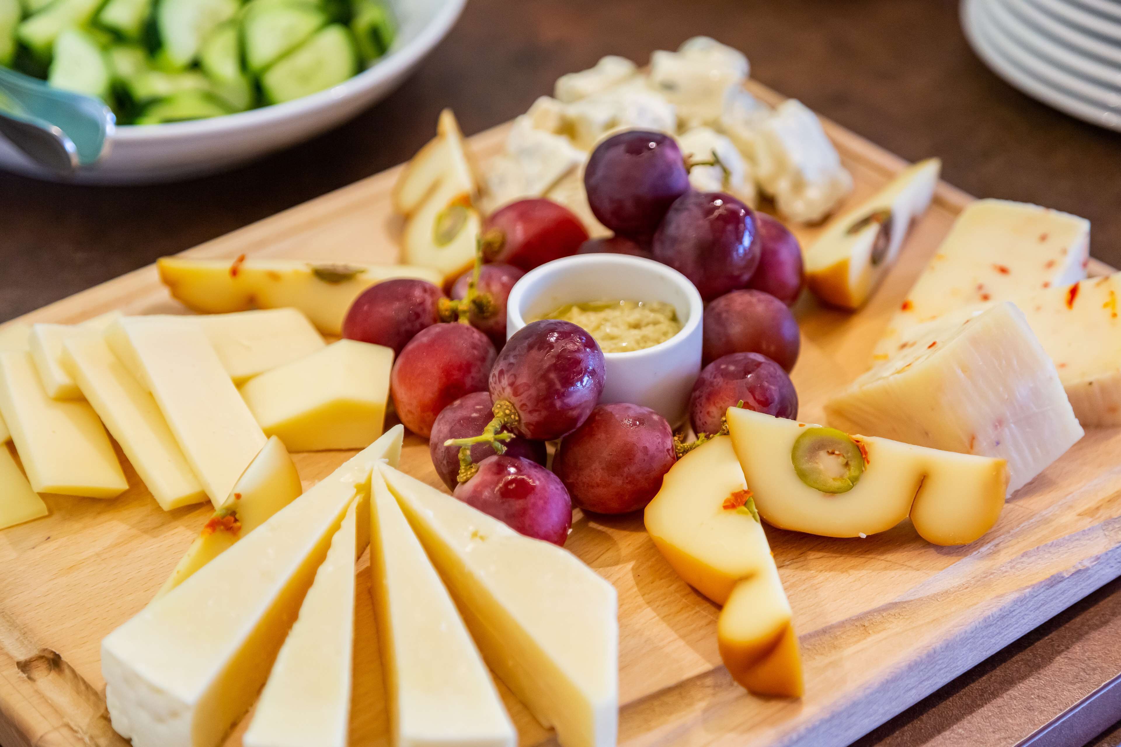 A wooden board with various cheeses, grapes, and a small bowl of dip.