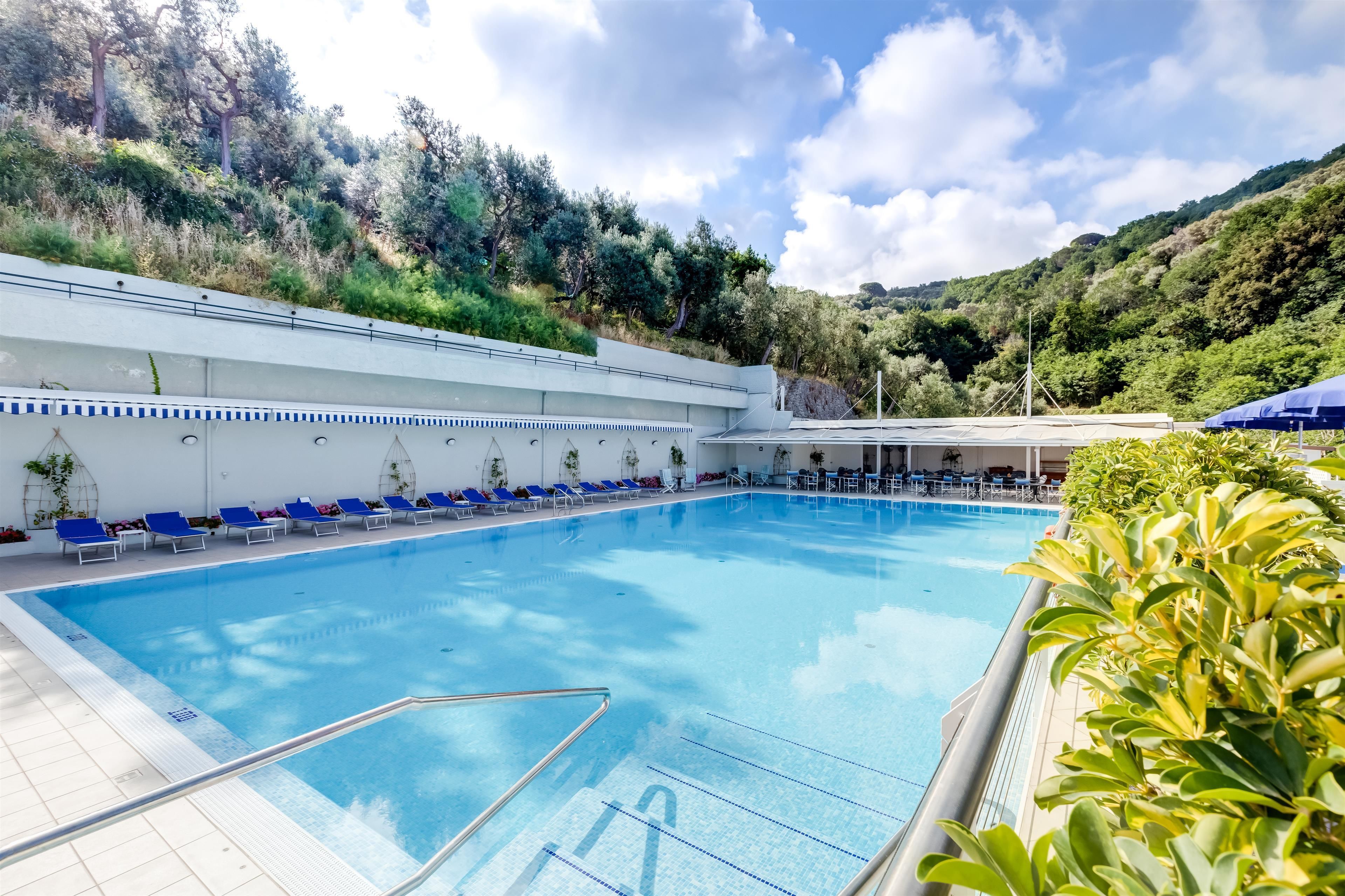 Una piscina con sillas azules, una sombrilla y vistas a una ladera.