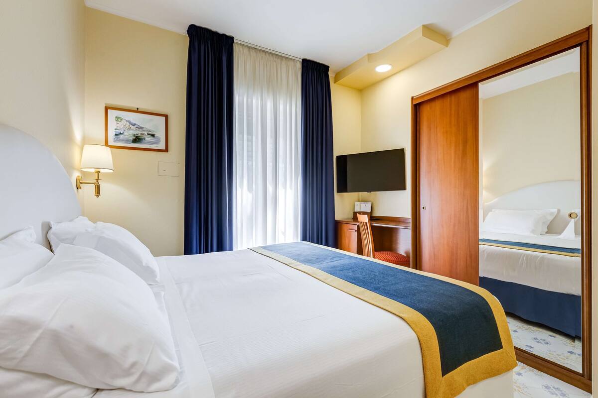 Een hotelkamer met een groot bed, een bureau met stoel, een televisie en een kledingkast.
