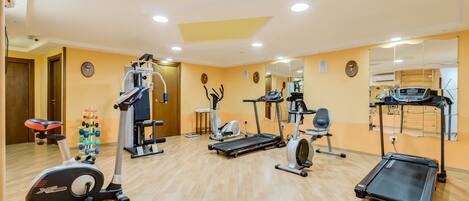 Un gimnasio con diversos equipos de ejercicio, incluyendo cintas de correr, una elíptica y una bicicleta estática.