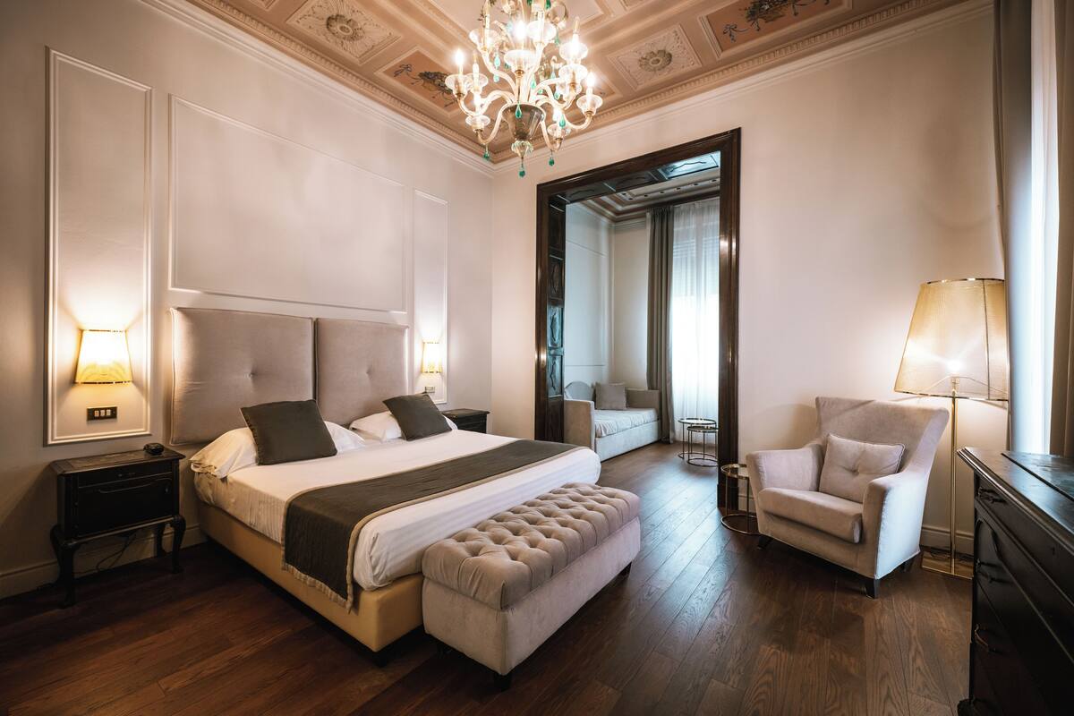 Een ruime slaapkamer met een groot bed, een zithoek en een kroonluchter.