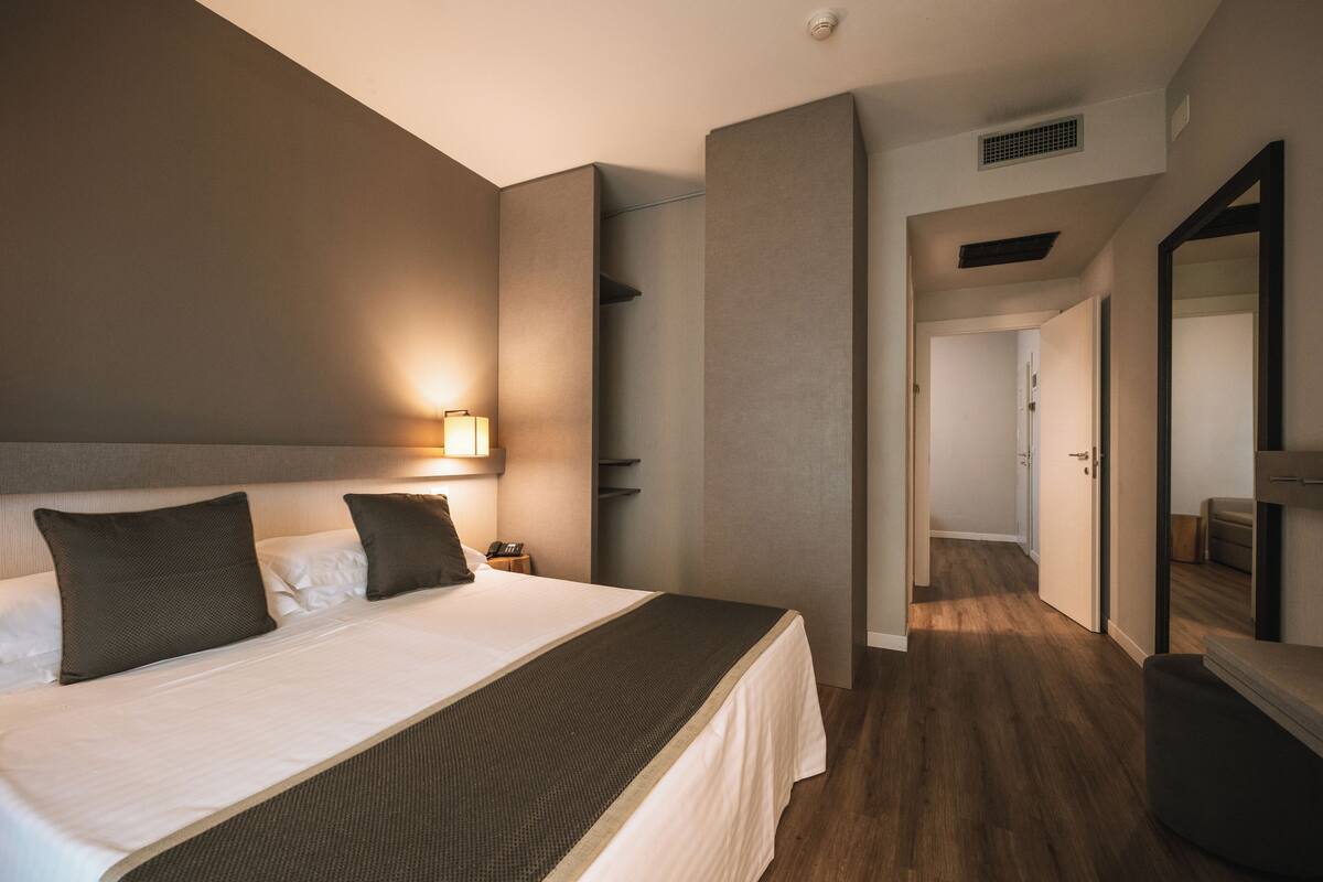 Een moderne hotelkamer met een groot bed, een bedlampje en uitzicht op de hal.
