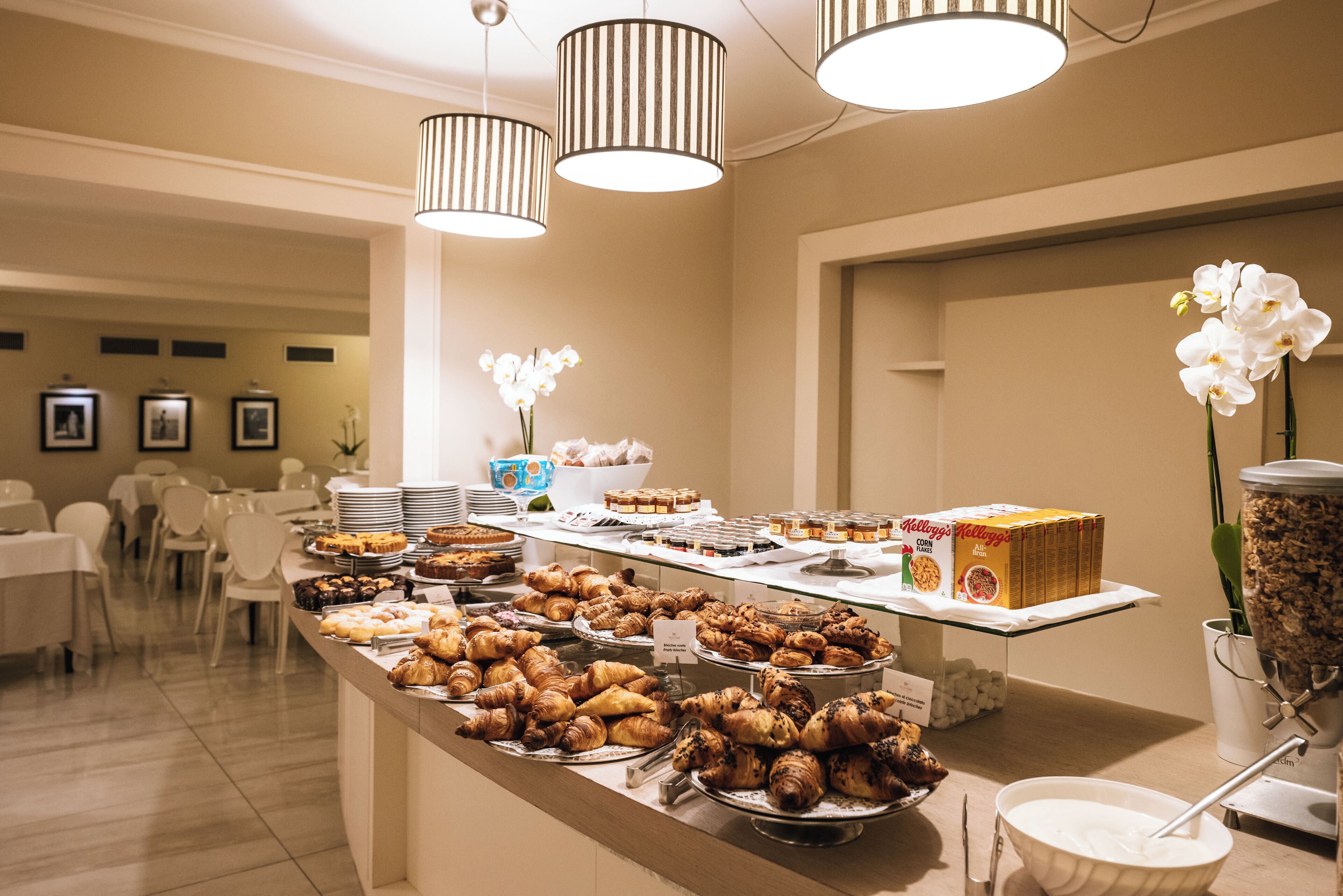 A buffet with various pastries and desserts, a coffee station, and a flower arrangement.