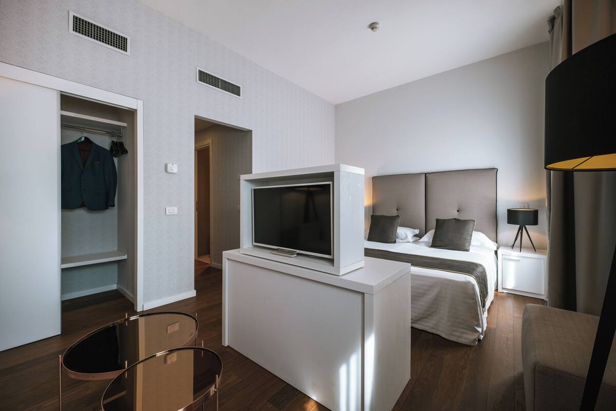 Een moderne hotelkamer met een bed, een televisie op een standaard, een kledingkast en een bureau met een lamp.