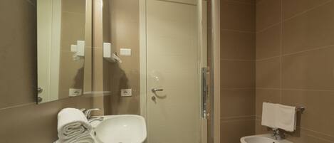 A modern bathroom with a glass shower enclosure, a white sink, a bidet, and a toilet.