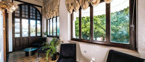 A spacious room with a patterned floor, large windows with curtains, and a potted plant.