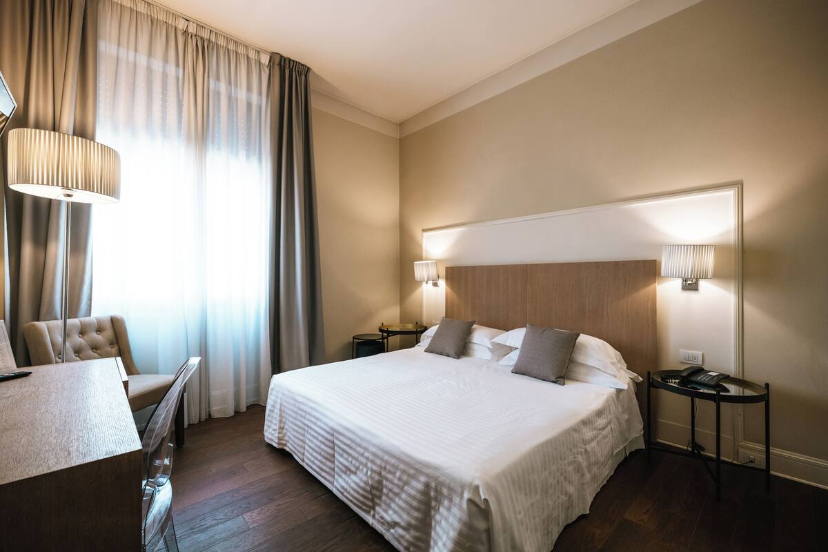 Een hotelkamer met een groot bed, een bureau met stoel, een lamp en een nachtkastje met telefoon.