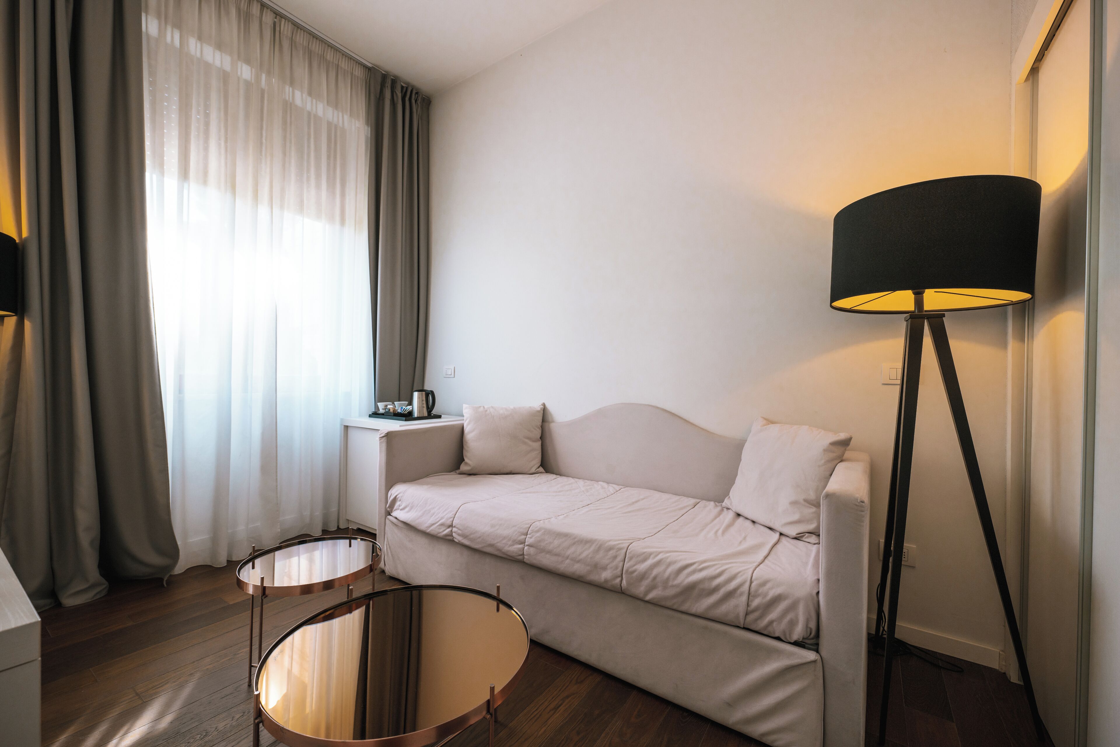 A modern living room with a sofa, two round tables, a floor lamp, and a window with curtains.