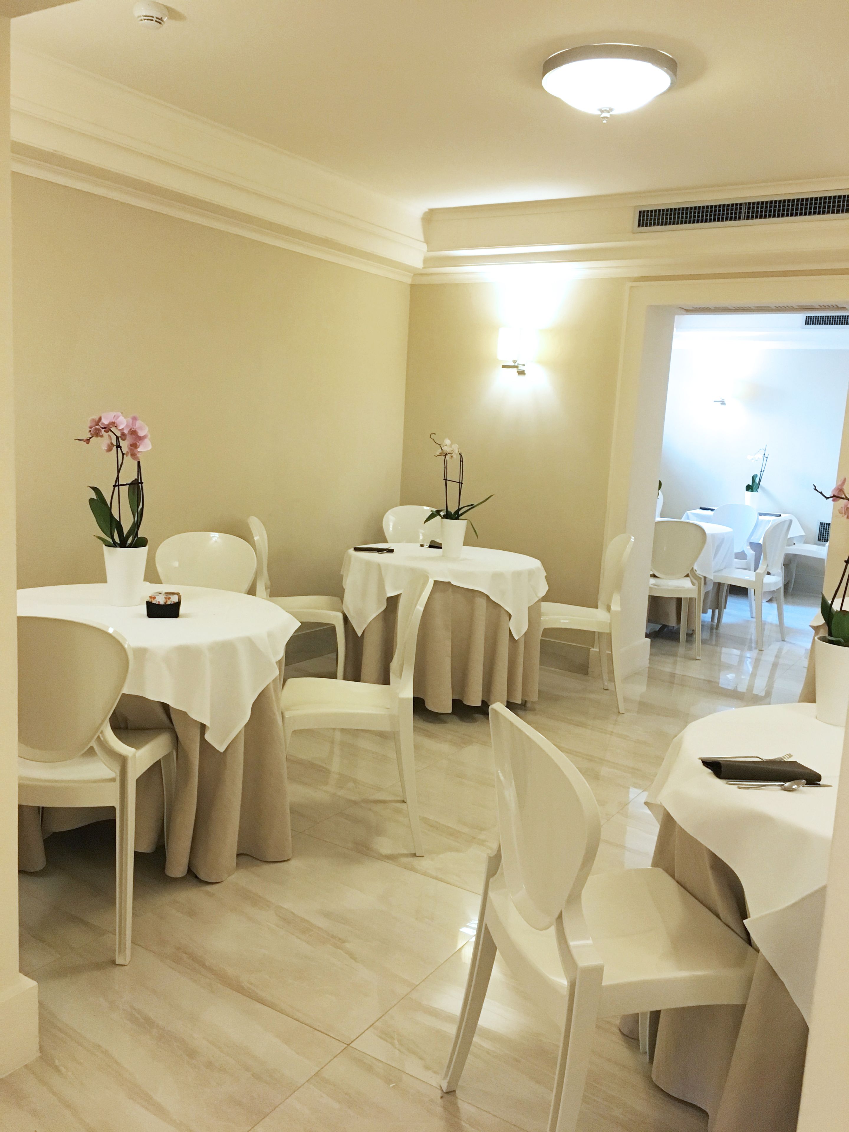 Comedor con mesas redondas, sillas blancas y orquídeas en macetas.