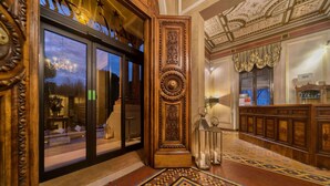 An ornate lobby with a patterned carpet, a wooden reception desk, and a chandelier.