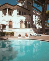 Zona de piscina con sillones de descanso y un edificio de arquitectura clásica.