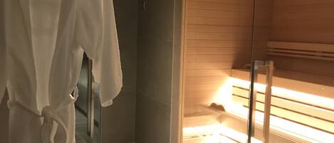 A modern bathroom with a glass shower enclosure, a robe hanging on a rack, and a tiled floor.
