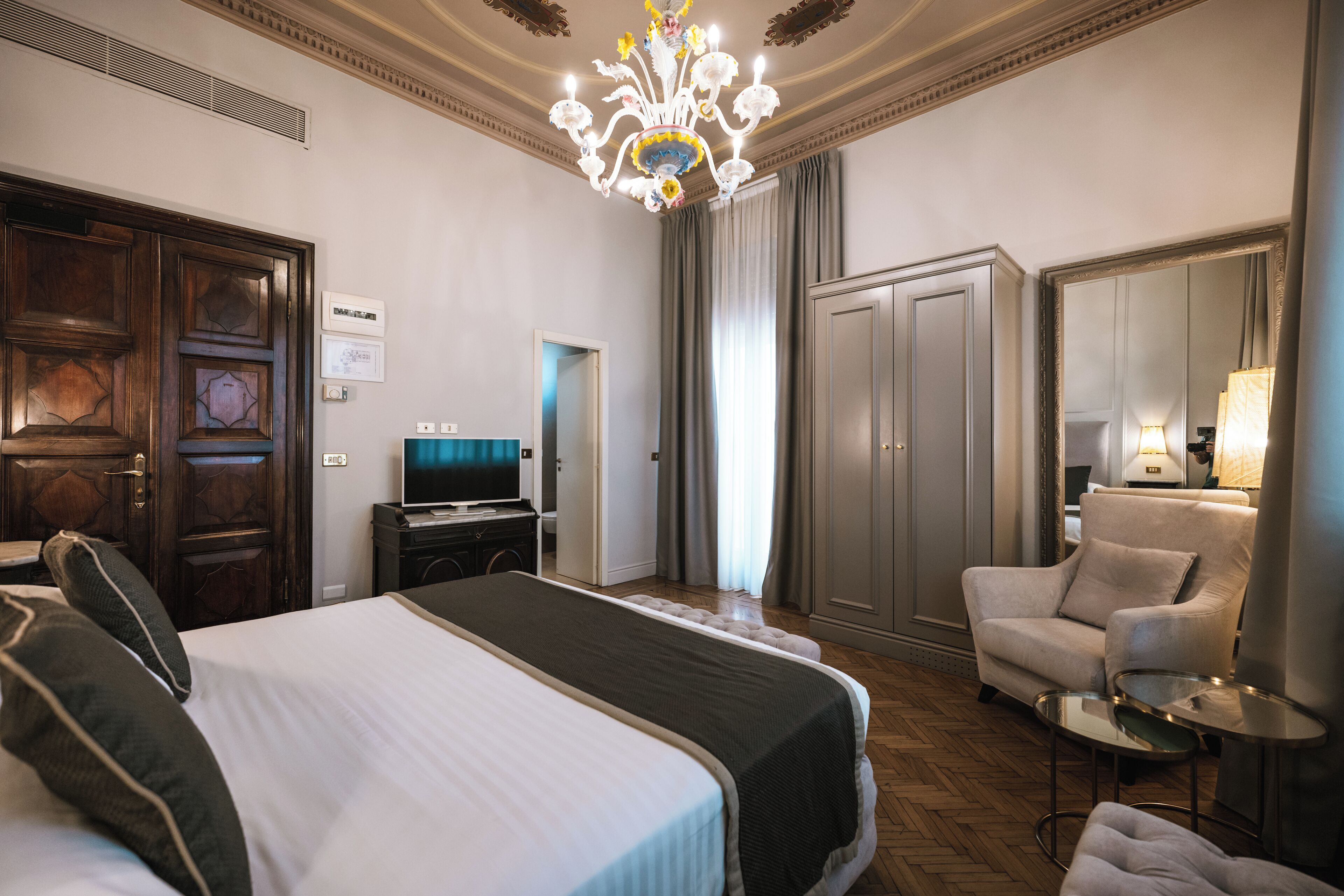 A hotel room with a large bed, a TV, a desk, a chair, and a wardrobe.