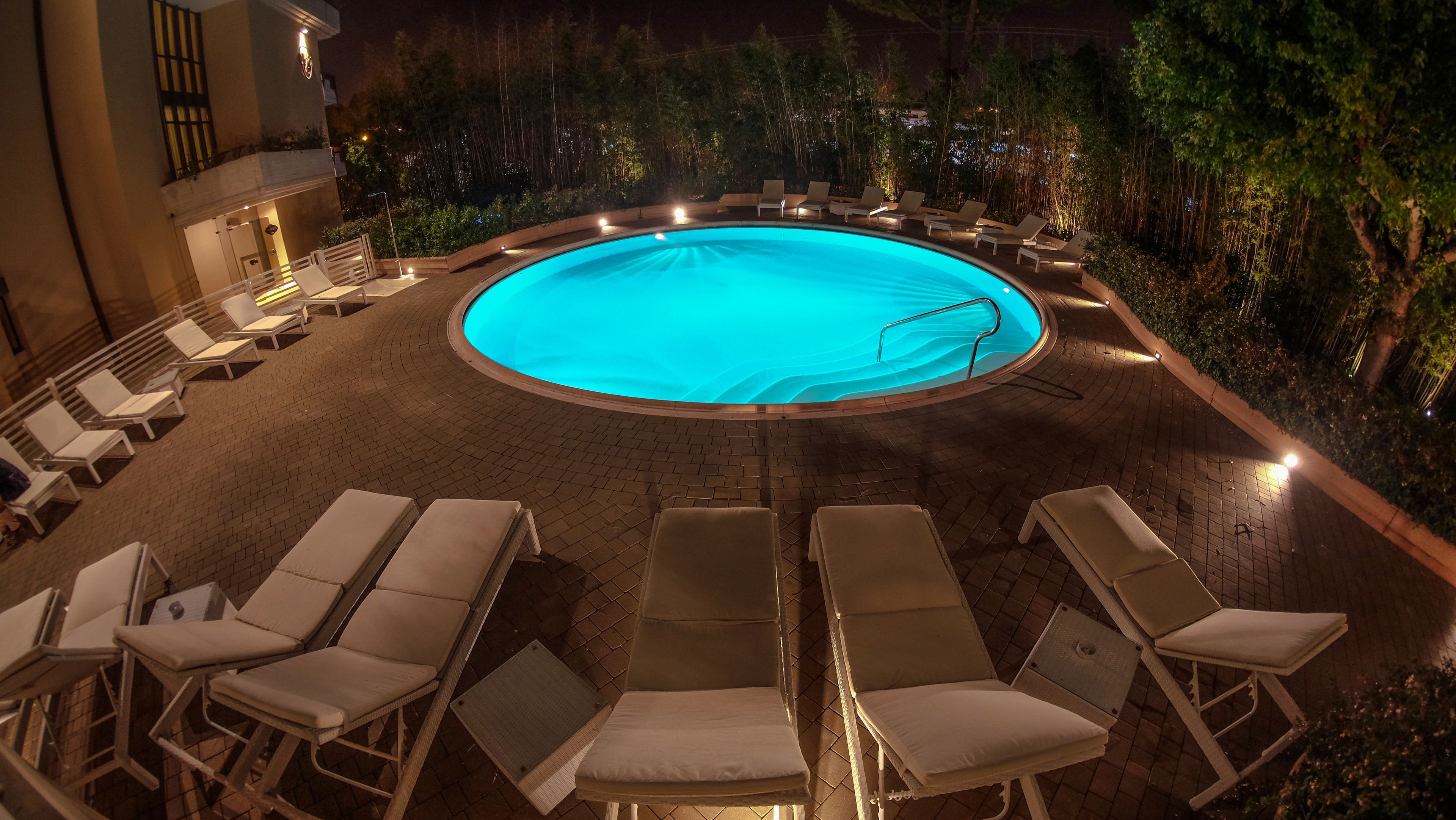 A circular pool with lounge chairs around it, surrounded by trees and a building.