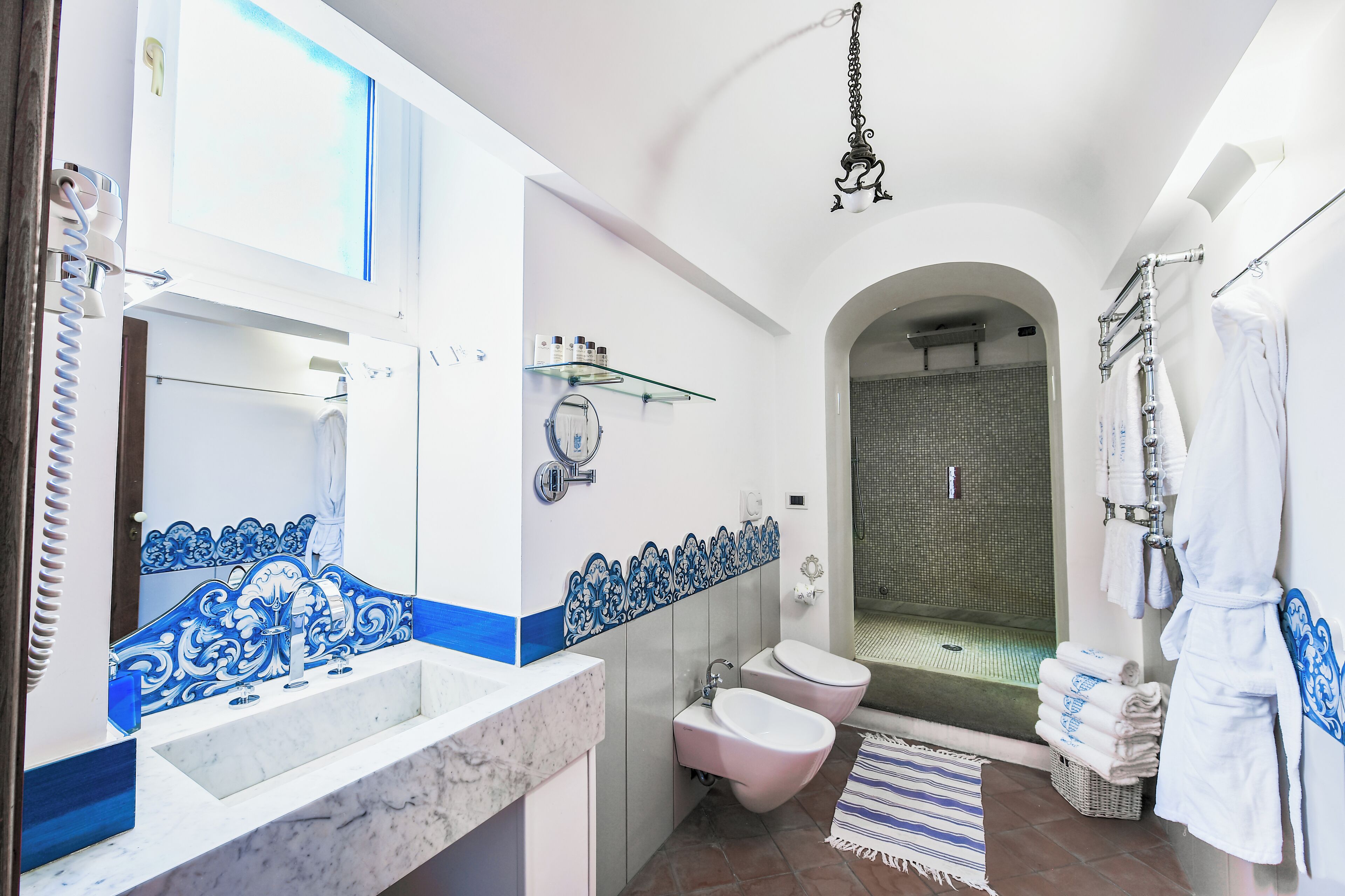 A bathroom with a marble sink, two toilets, a glass shower enclosure, and a hanging bathrobe rack.