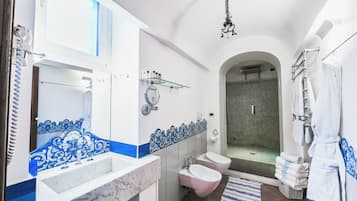 A bathroom with a marble sink, two toilets, a glass shower enclosure, and a hanging bathrobe rack.