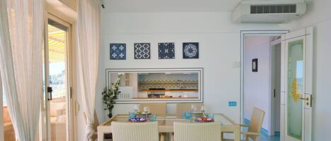 Un coin repas avec des chaises en osier, une table à plateau en verre et un miroir décoratif au-dessus.