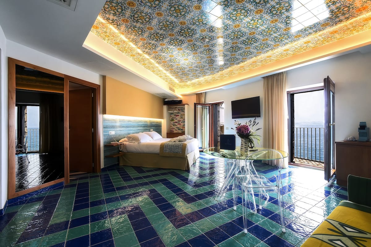 Une chambre d’hôtel avec un lit, une table en verre, un balcon avec vue et un sol carrelé.