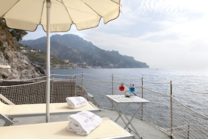 Relax on this seaside terrace with ocean views and a mountainous backdrop, featuring a comfortable seating area and secure barrier.