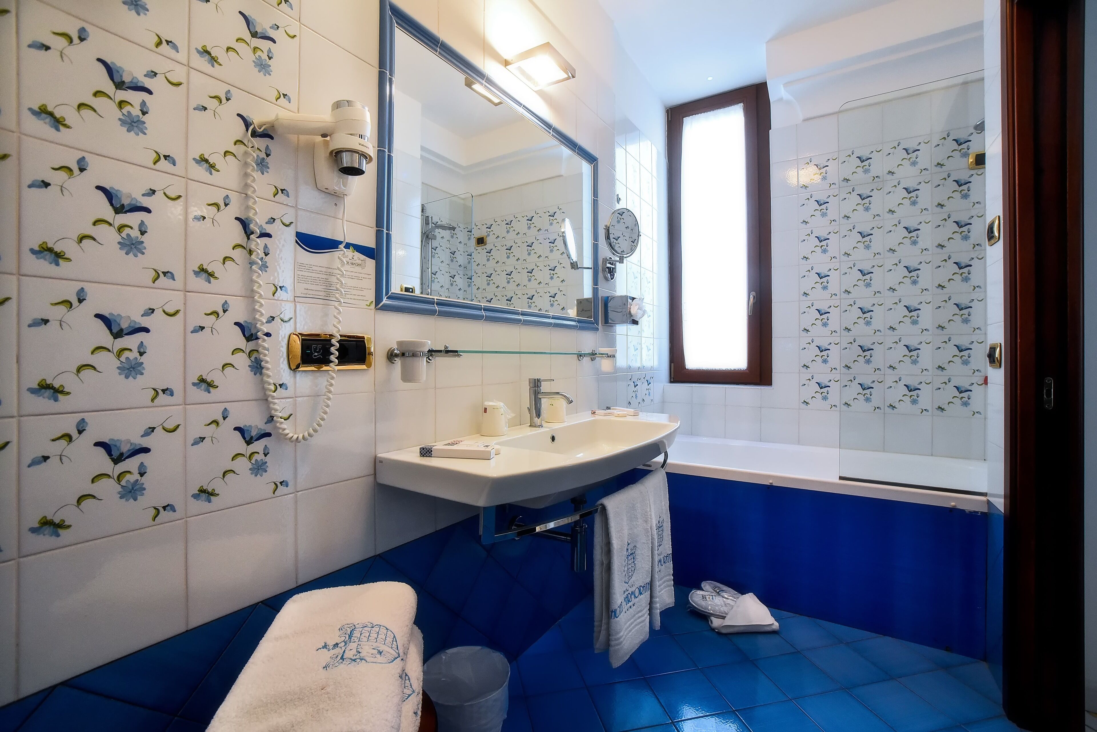 A bathroom with a white sink, blue tiles, a mirror, and a shower area.