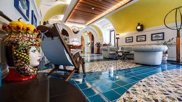 A spacious lobby with a tiled floor, a wooden ceiling, and a seating area with a sofa and armchairs.