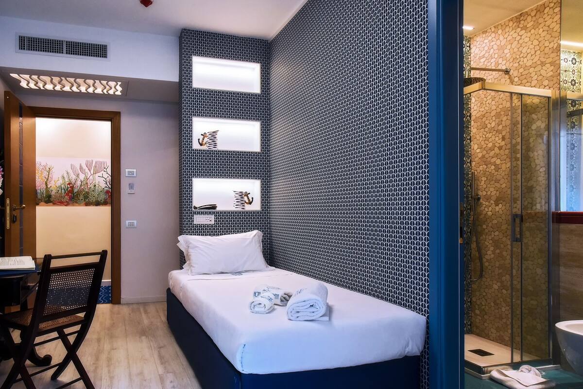 Une chambre d’hôtel de taille réduite, comprenant un lit, un bureau et un espace douche.